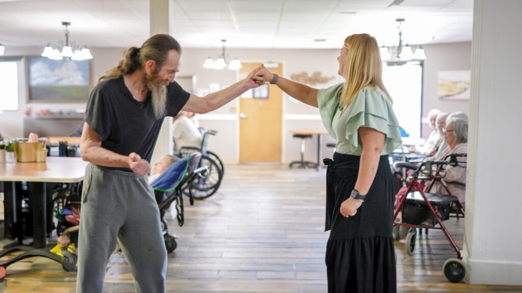 A man and a woman dance at a skilled nursing facility during an activity