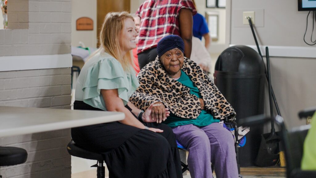 A woman and a nurse hold hands at a skilled nursing facility